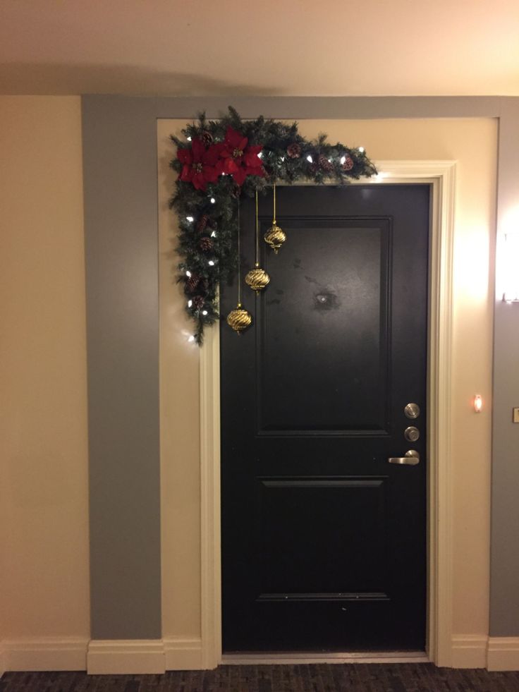 a black door with christmas decorations on the top and bottom, in front of a gray wall