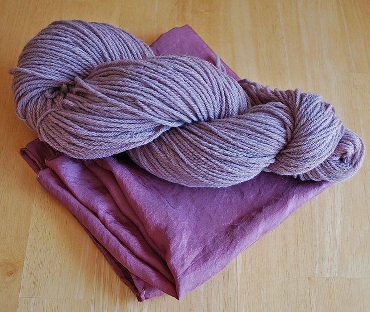 two skeins of yarn sitting on top of a purple piece of cloth next to each other