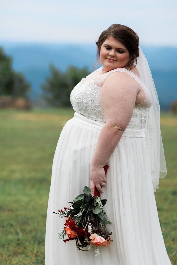 a woman in a white dress is holding a bouquet and posing for the camera with her hands on her hips