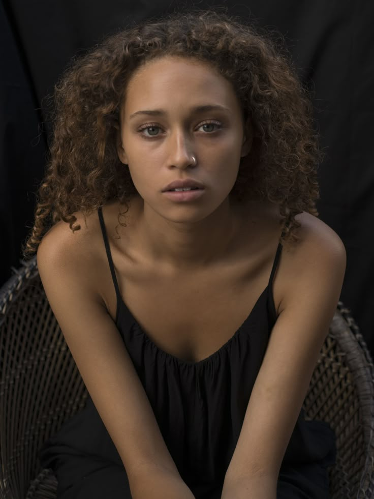 a woman sitting in a wicker chair with her hands on her knees looking at the camera