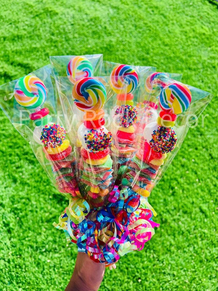 a hand holding candy lollipops on top of green grass