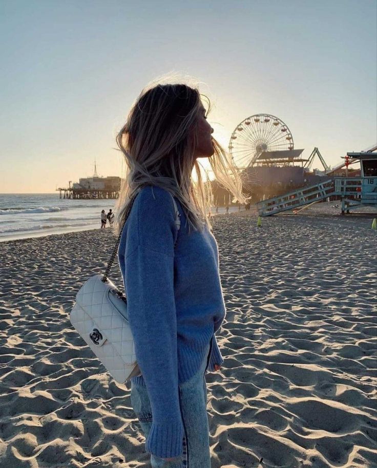 a woman standing on top of a sandy beach next to the ocean with ferris wheel in the background