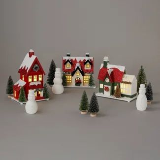 a group of small christmas houses with lights on and trees in the snow around them