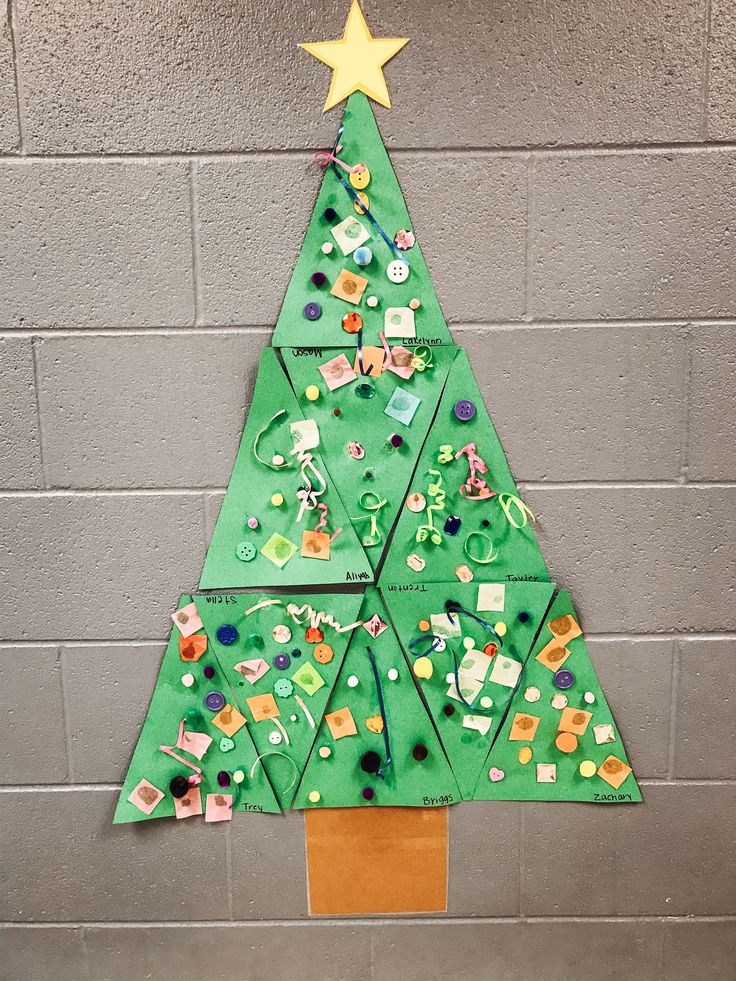 a christmas tree made out of green paper on a gray brick wall with a star hanging from the top