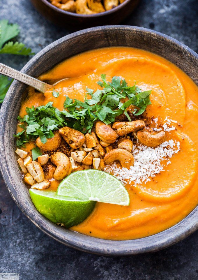 a bowl filled with carrot soup and garnished with cilantro, parsley and lime