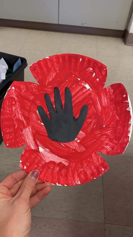 someone is holding up a paper plate with a handprinted poppy flower on it