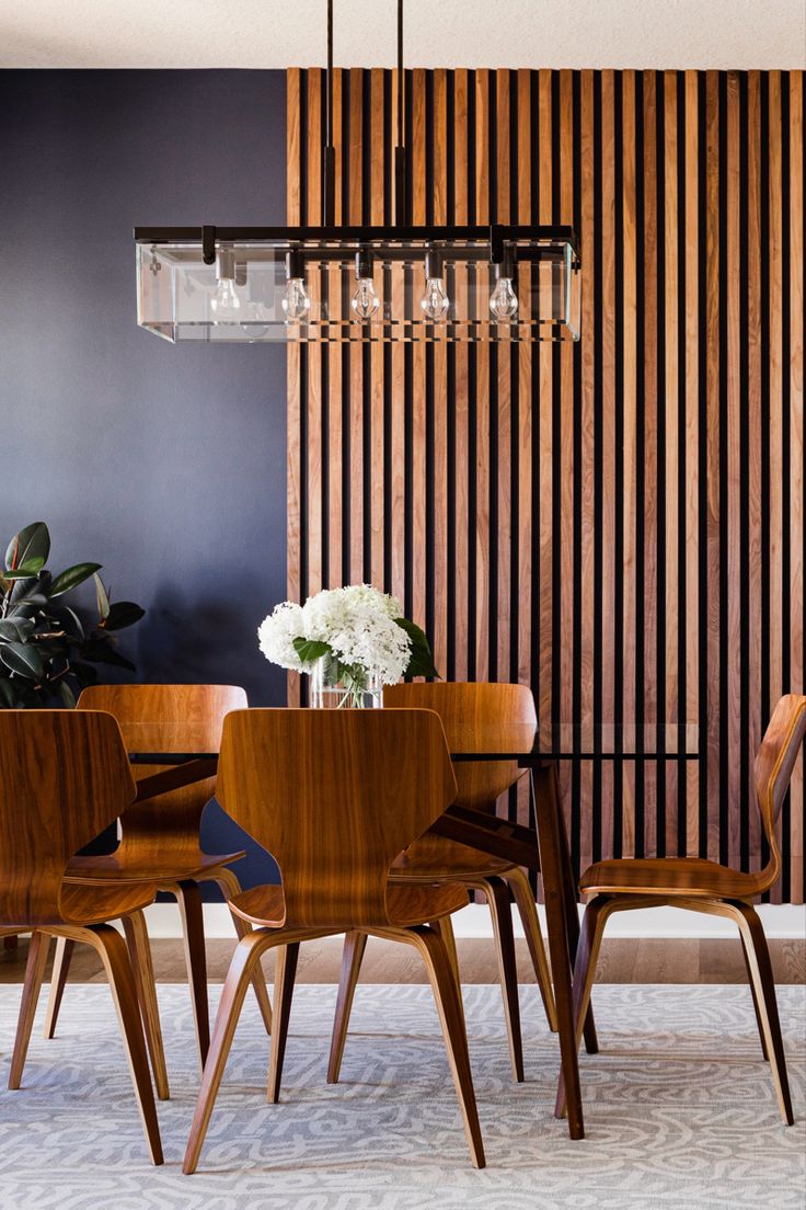 a dining room table and chairs in front of a wooden wall with vertical slats