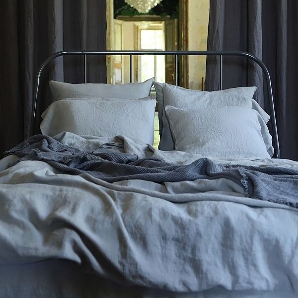 an unmade bed with white linens in front of a mirror and chandelier