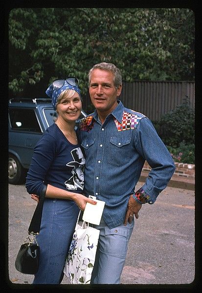 a man and woman standing next to each other in front of a car with trees behind them