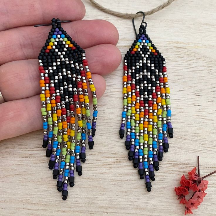 a pair of multicolored beaded earrings is being held by a hand