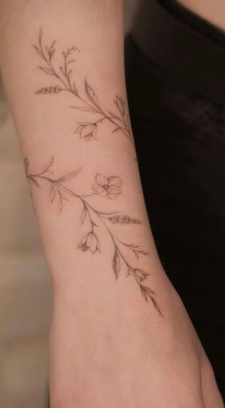 a woman's arm with flowers and leaves tattooed on her left wrist, in black ink