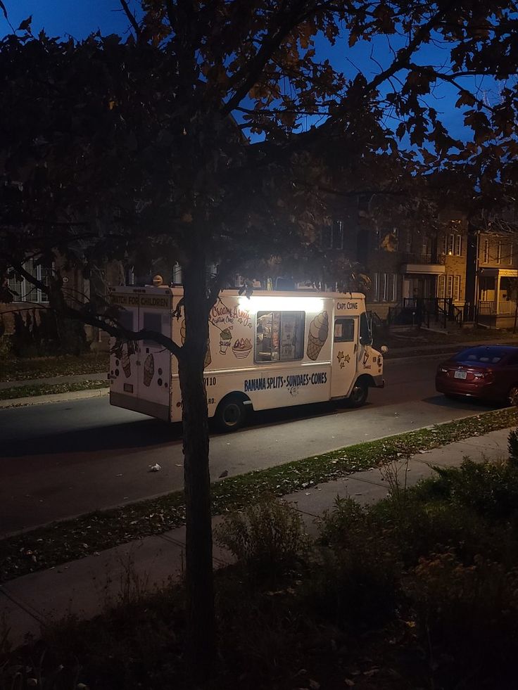 an ice cream truck parked on the side of the road at night with its lights on