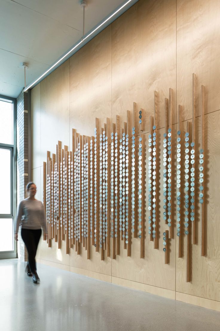 a woman walking past a wooden wall with circles on it in front of a large window