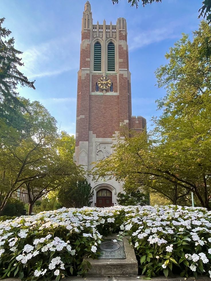 a tall tower with a clock on the side of it surrounded by trees and flowers