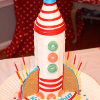 a young boy sitting at a table in front of a cake with a rocket on it