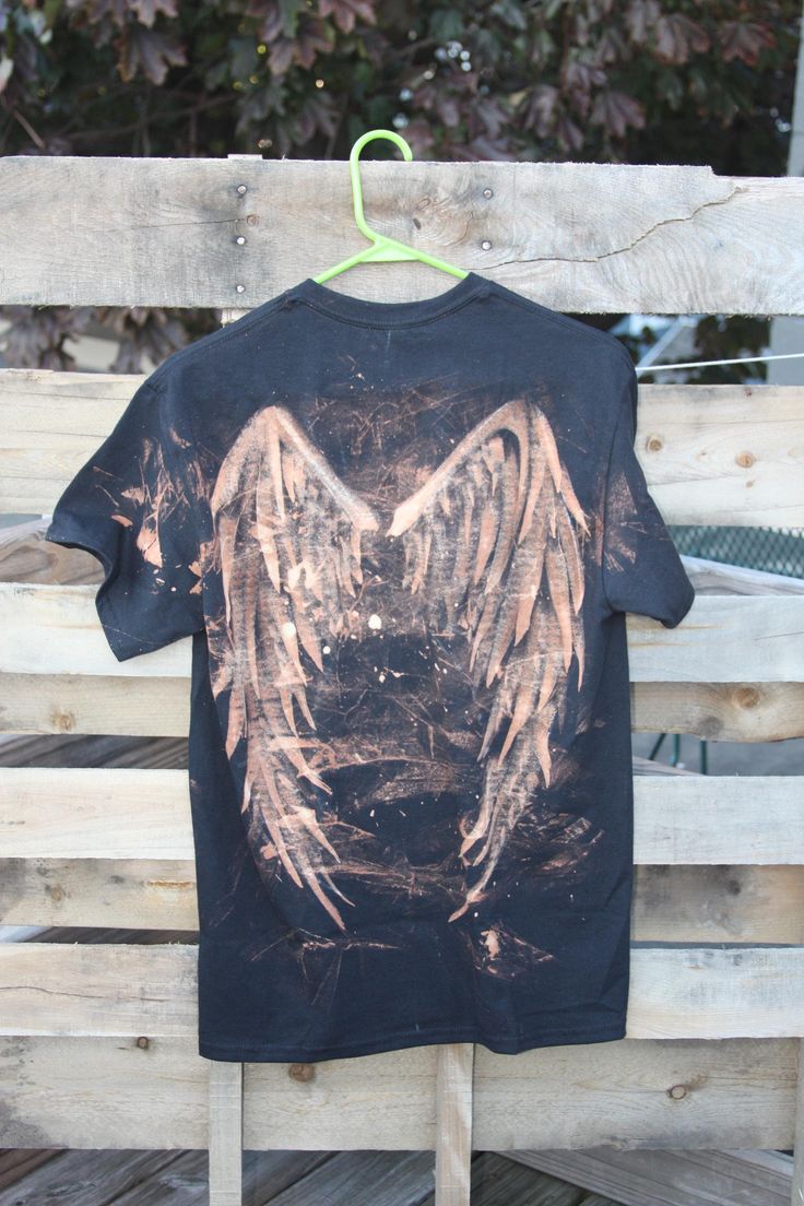 a t - shirt with an angel design hanging on a wooden bench