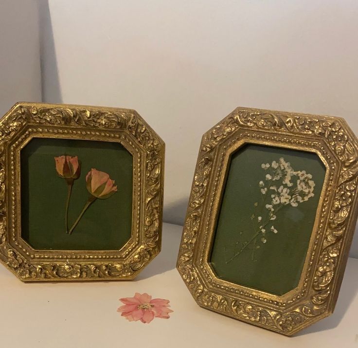 two gold frames with flowers in them sitting on a table