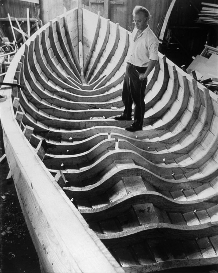 a man standing on top of a boat made out of wooden planks in a factory