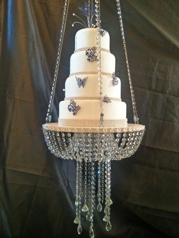 a three tiered wedding cake with butterflies on the top is suspended from a chandelier