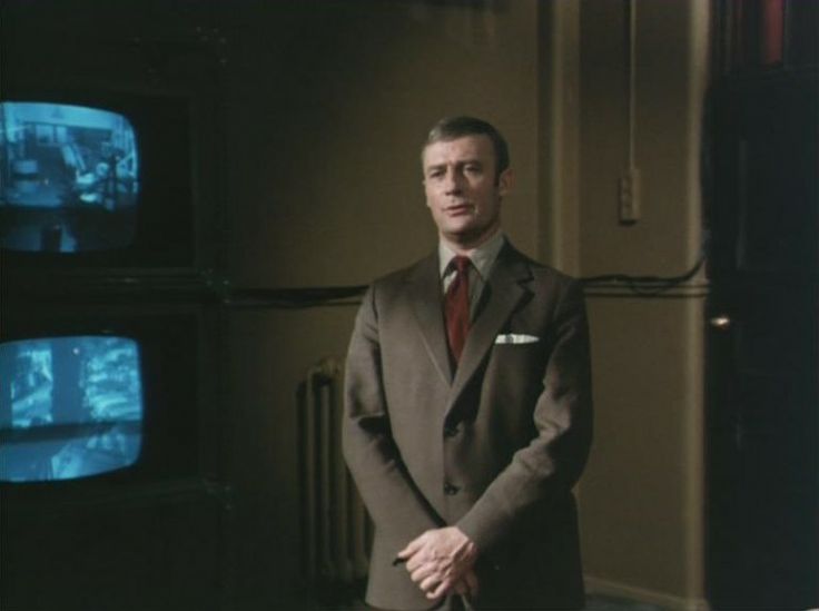 a man in a suit and tie standing in front of televisions with their hands on his hips