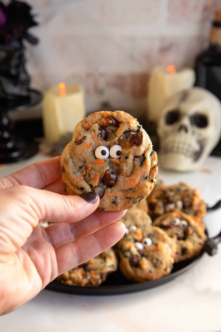 a hand holding up a cookie with eyes and googly eyes in front of other cookies