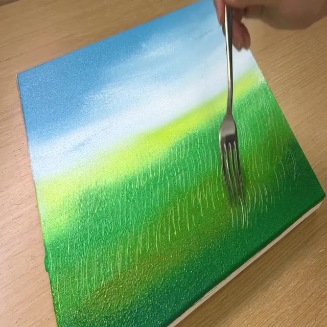 a person holding a fork and painting on a piece of paper with green grass in the background