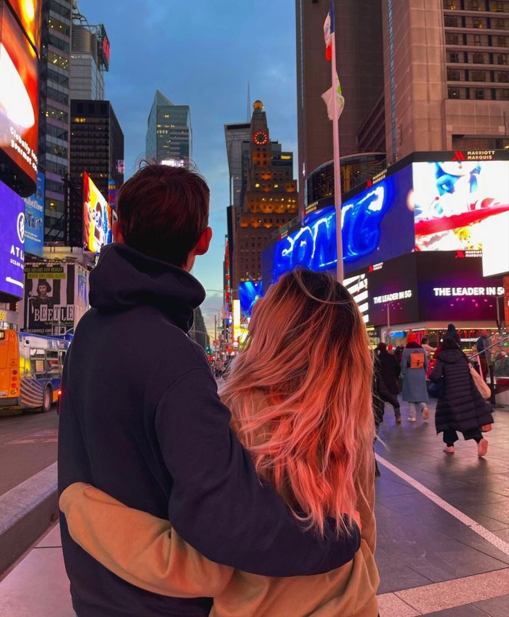 a man and woman standing in the middle of a busy city street at night time