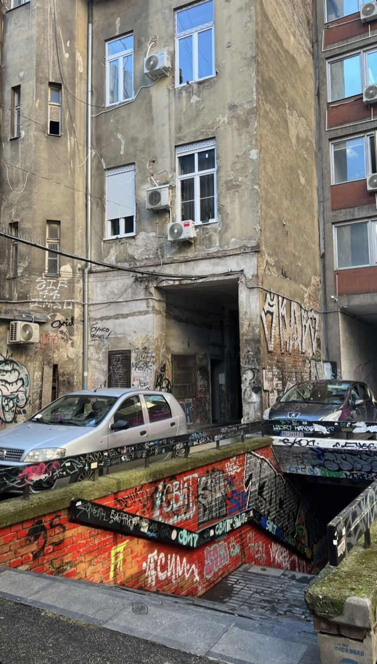 an old building with graffiti on it and cars parked in the street next to it