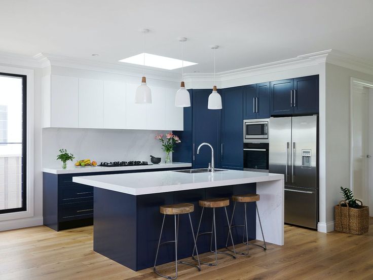 a large kitchen with blue cabinets and white counter tops, two stools at the island