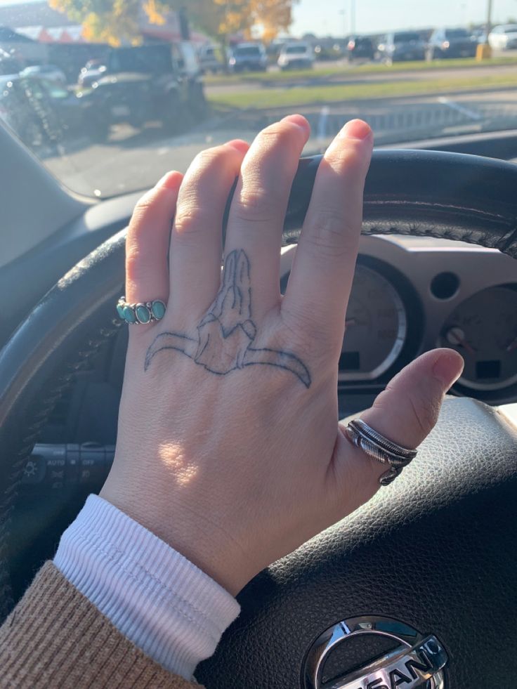 a person's hand on the steering wheel of a car, with an arrow tattoo