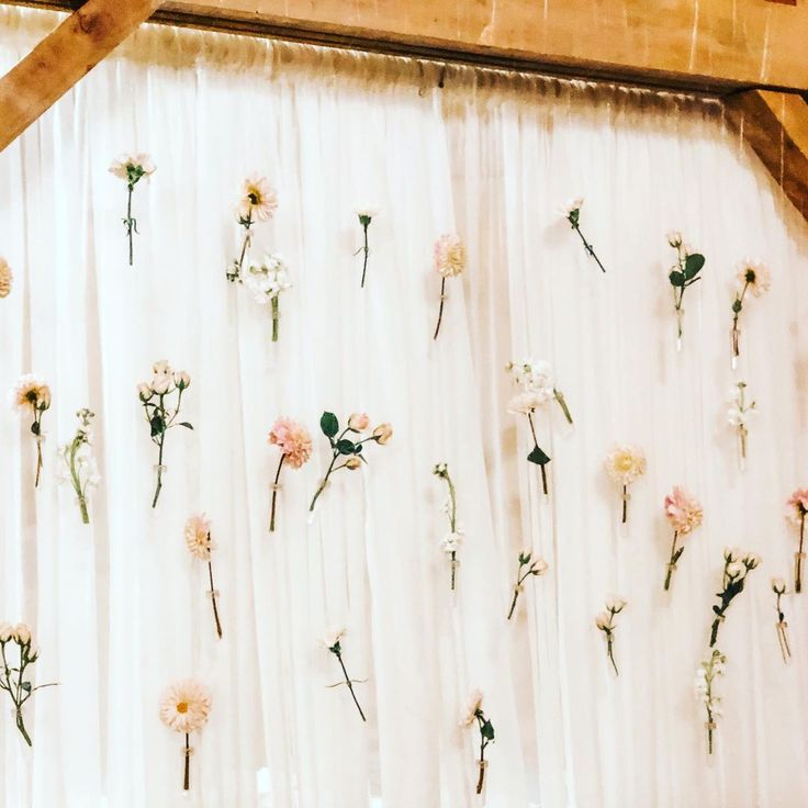 flowers are arranged on the side of a white wall with sheer drapes behind them