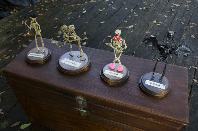 five skeleton figurines are sitting on top of a wooden box, each with their own name