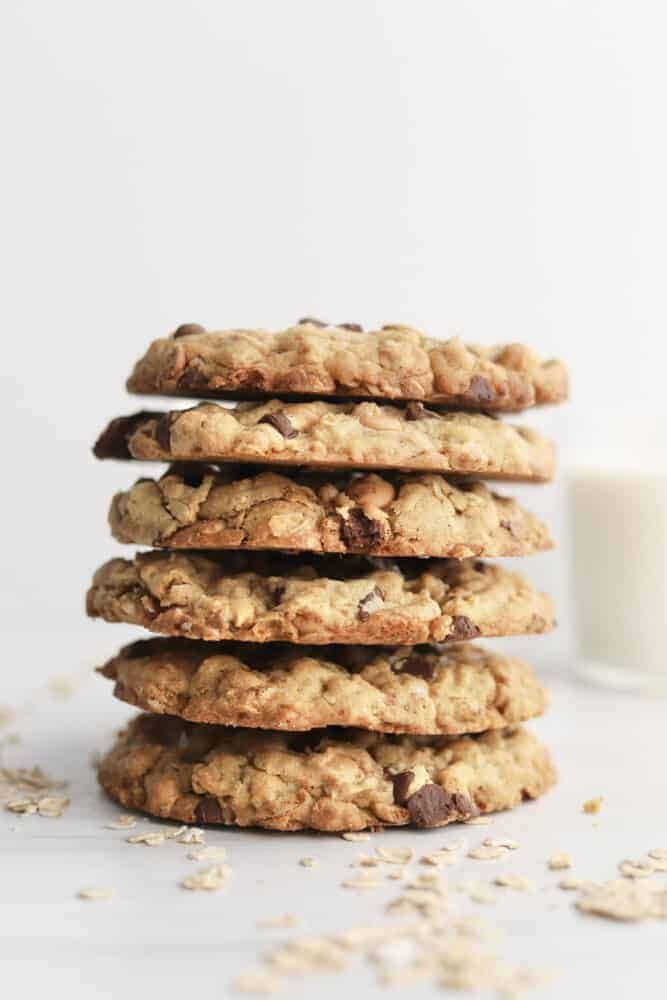 a stack of oatmeal cookies next to a glass of milk on a white surface