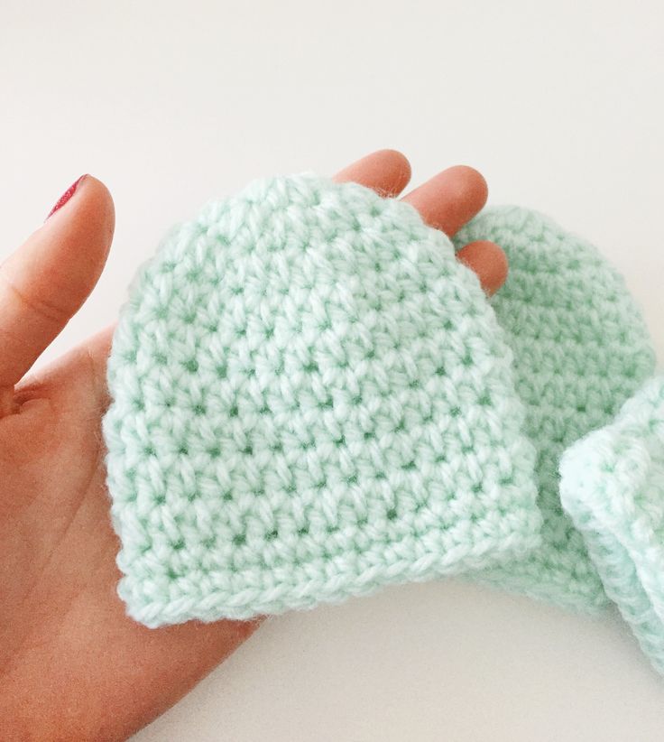 a hand holding a green crocheted mitt on top of a white table