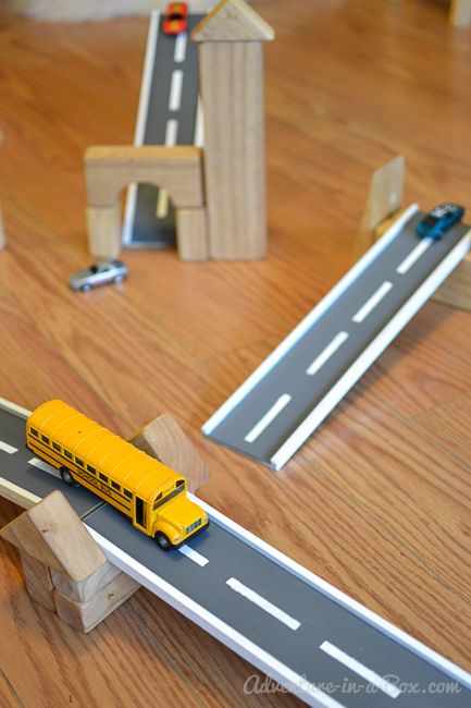 a toy school bus is on the road next to wooden blocks and cars that are sitting on the floor