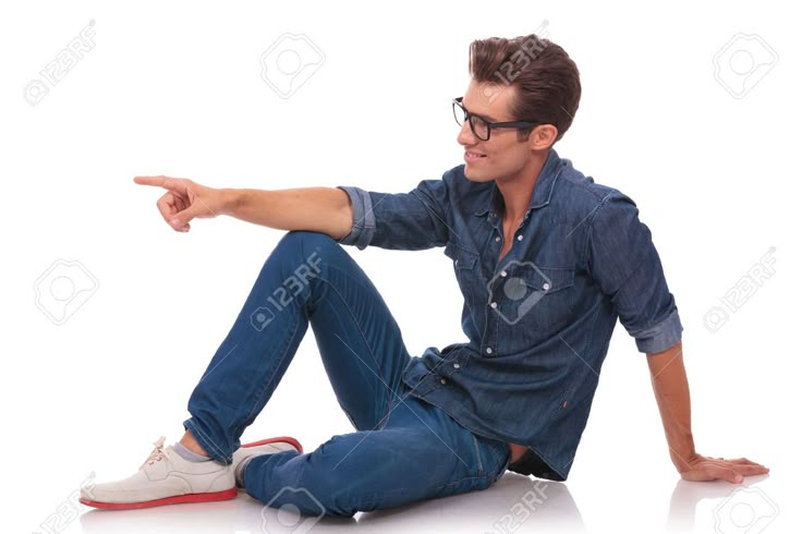 a young man sitting on the floor pointing at something with his hand and wearing glasses