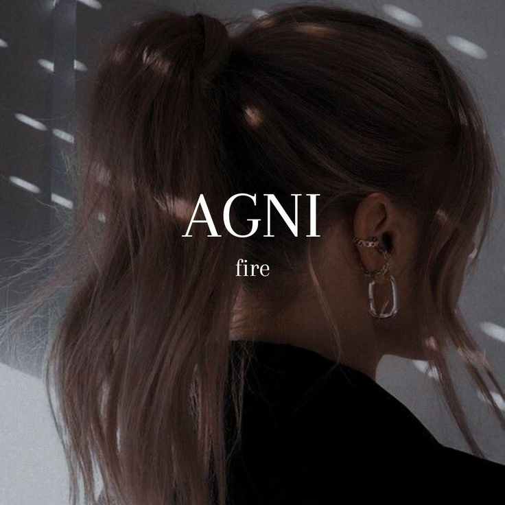 a woman with long hair and hoop earrings in front of a wall that says agni fire