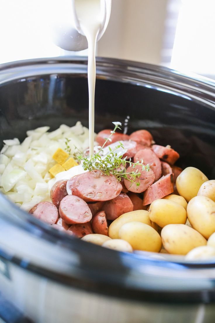 a crock pot filled with potatoes, ham and gravy being poured into the slow cooker