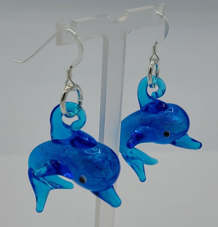 A blue glass dolphin charm that is 1 1/4 inches high and 1 1/4 inches wide was used to make this pair of earrings.  The earrings hang a total of 2 inches in length and have a sterling silver earring wire. Blue Ocean-inspired Dangle Jewelry, Blue Fish Hook Earrings For Gift, Gift Blue Fish Hook Earrings, Blue Drop Earrings With Fish Hook, Resin Dolphin Earrings, Blue Dangle Earrings With Ocean-inspired Style, Adjustable Dangle Earrings Ocean-inspired, Horseshoe Earrings, Nickel-free Blue Glass Earrings