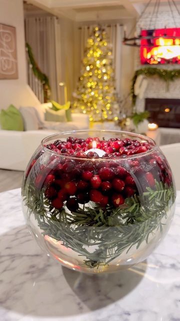 a glass bowl filled with cranberries and greenery on top of a table