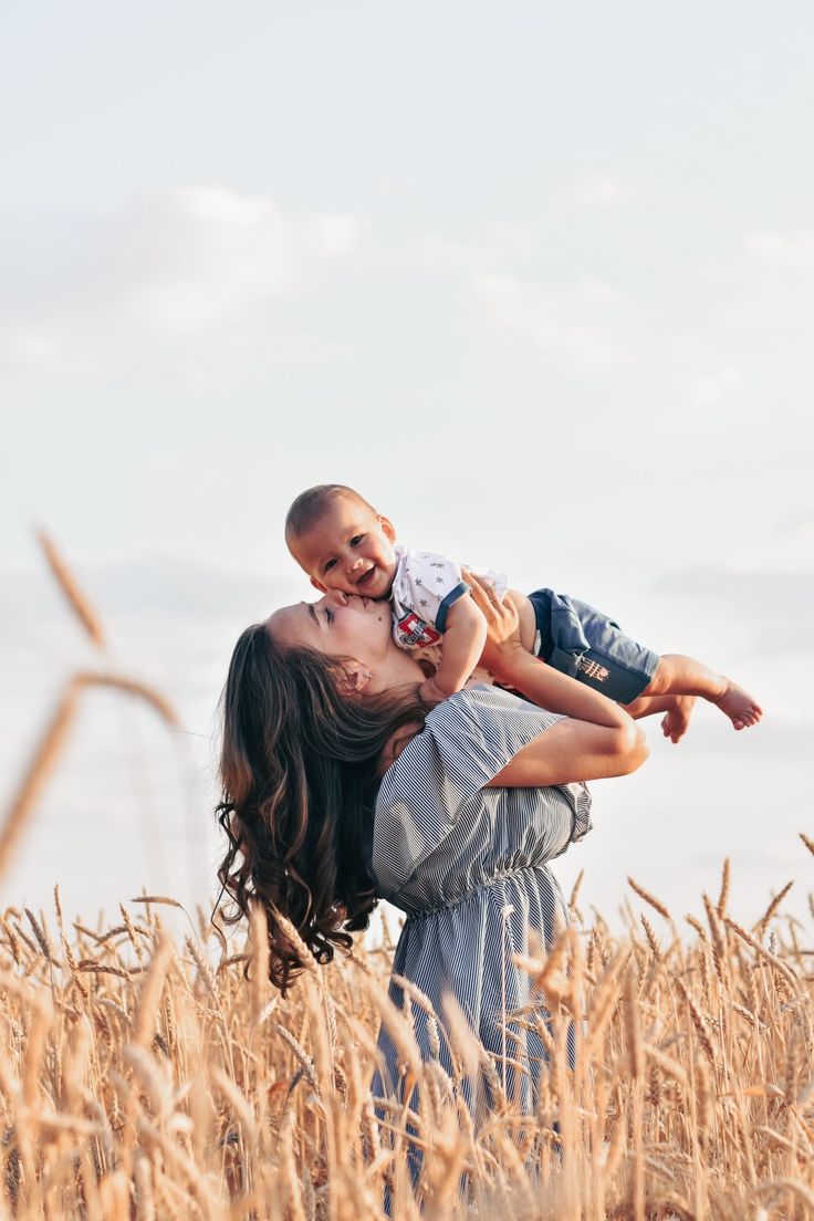 a woman holding a baby in her arms while standing in a wheat field