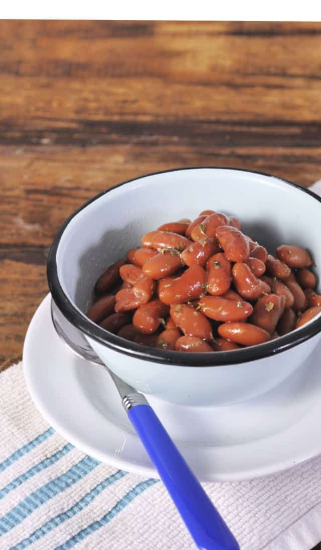 a white bowl filled with red beans on top of a plate next to a blue spoon