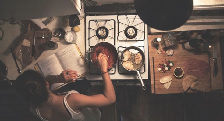 a woman is reading a book while cooking in the kitchen with an open cookbook