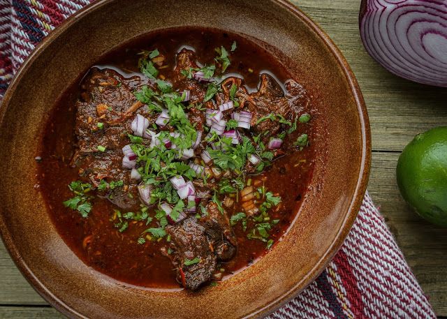 a brown bowl filled with meat and vegetables on top of a table next to an onion wedge