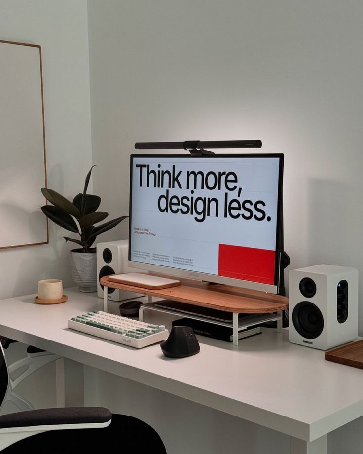 a desk with a monitor, keyboard and speakers on it that says think more design less