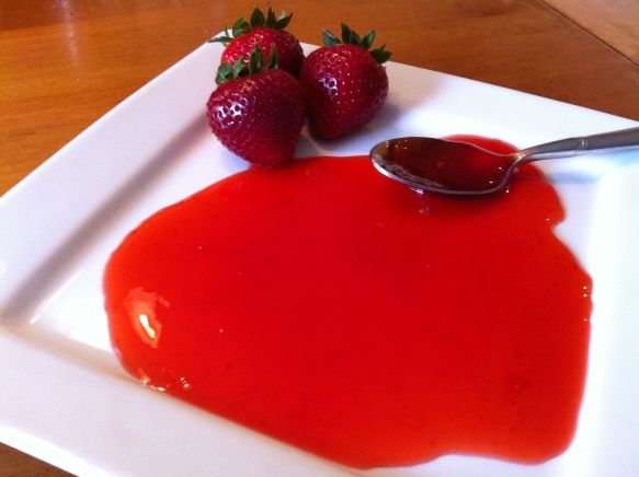 two strawberries on a white plate with red sauce