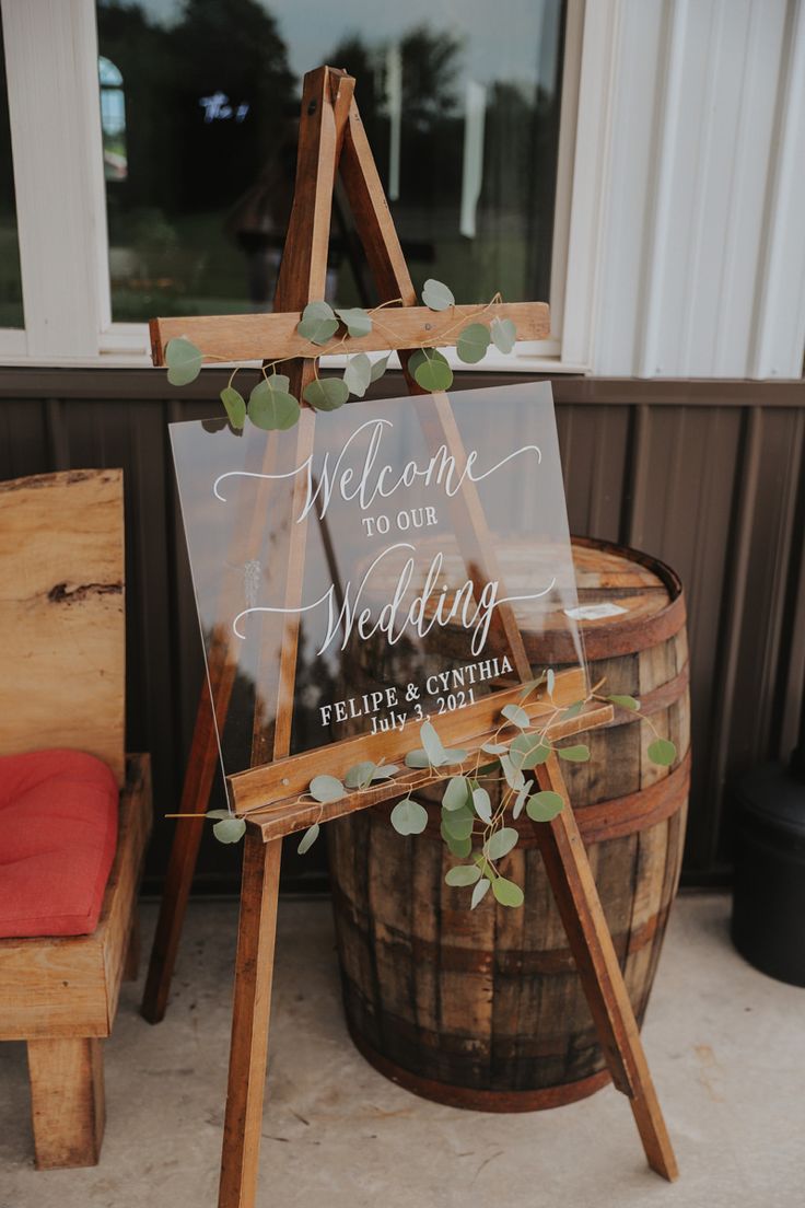 a wooden easer with a sign that says welcome to our wedding and eucalyptus leaves on it