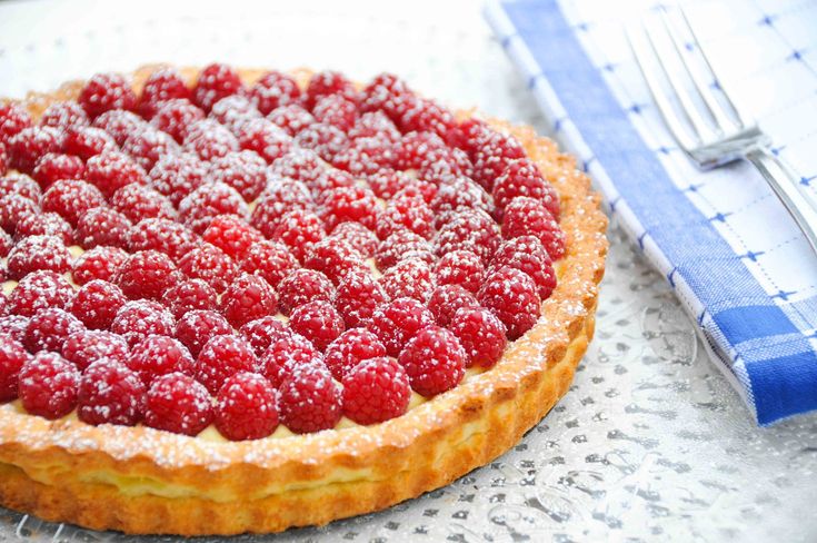 a cake with raspberries on top is sitting next to a fork and knife