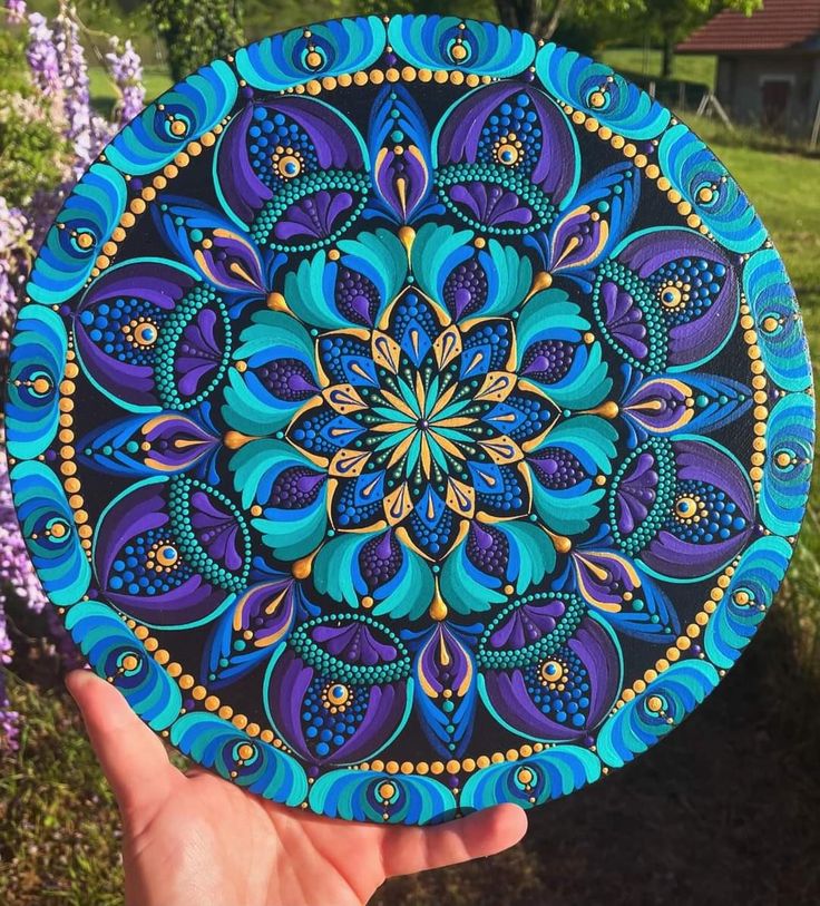 a hand holding up a blue and purple plate with an intricate design on the front