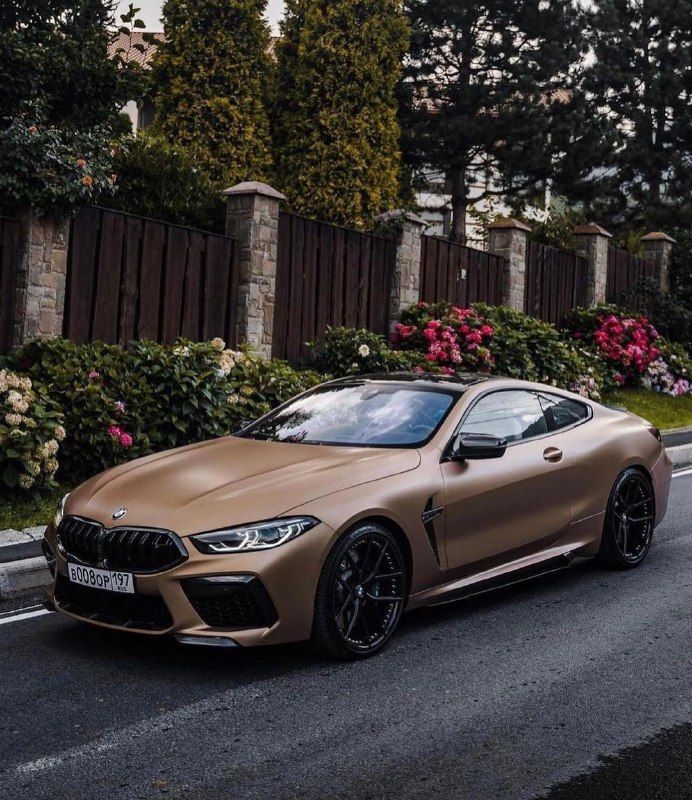 a tan bmw car parked on the side of the road with flowers in the background